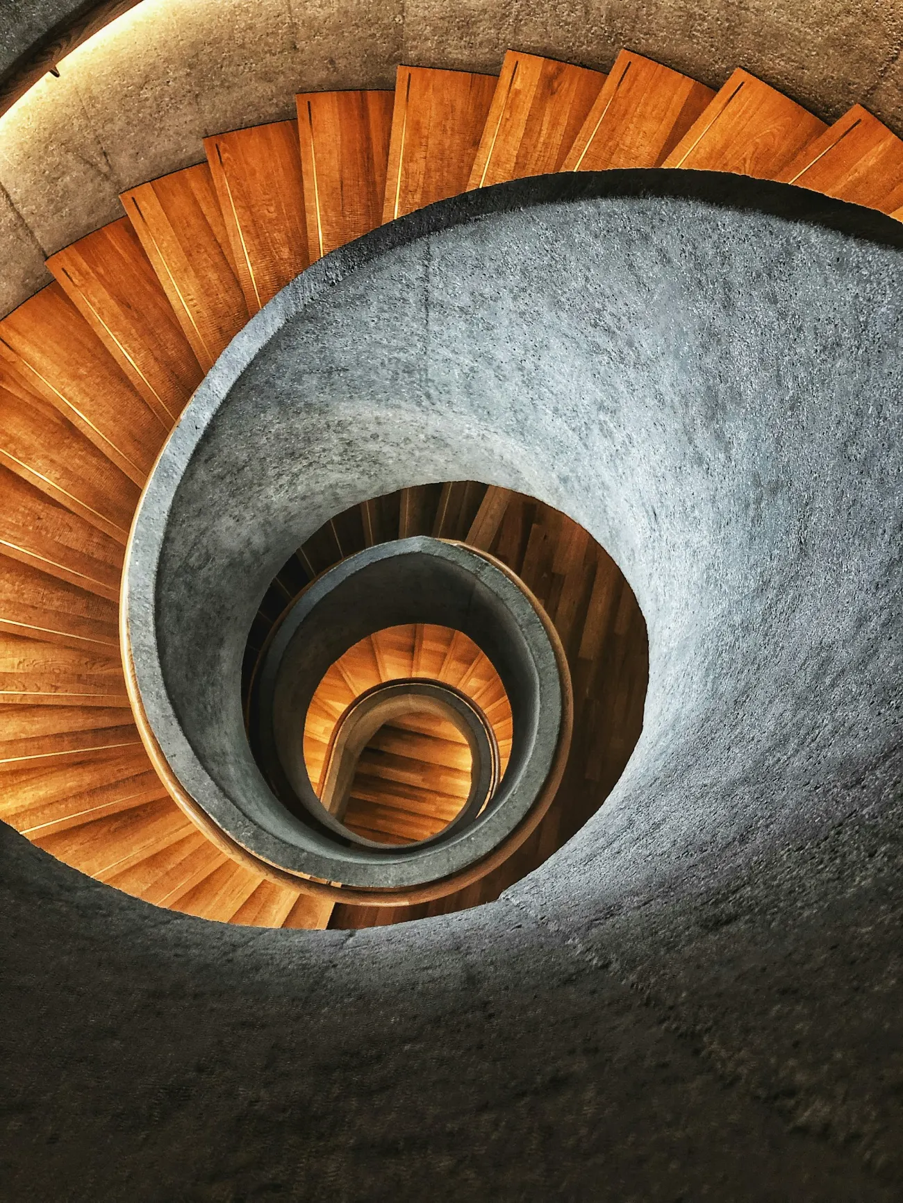 Scară în spirală văzută de sus, cu trepte de lemn care se repetă spre centru.